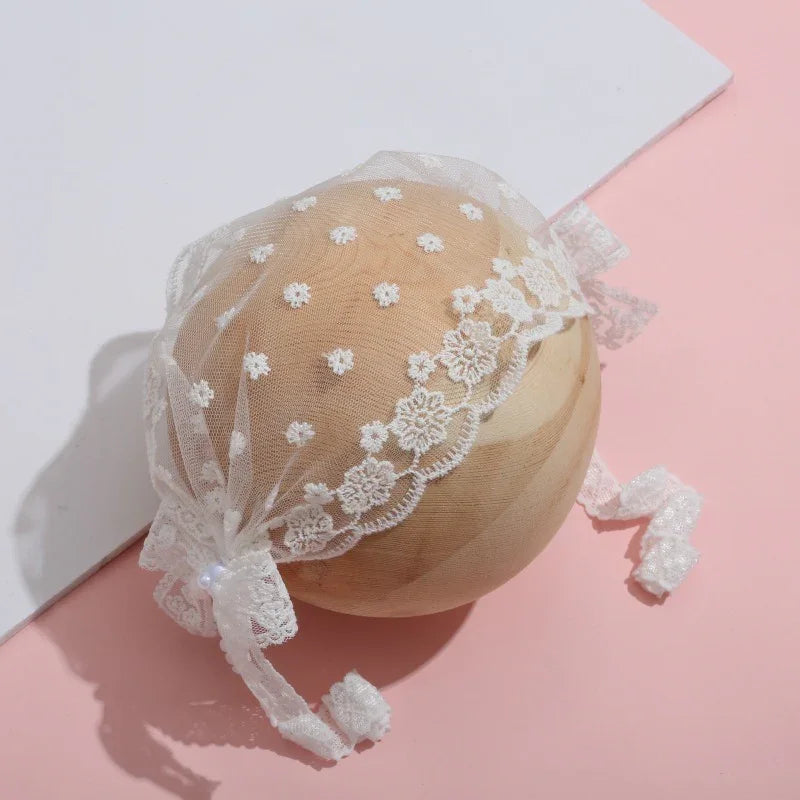 Delicate white lace bonnet with floral embroidery and ribbon ties on wooden sphere