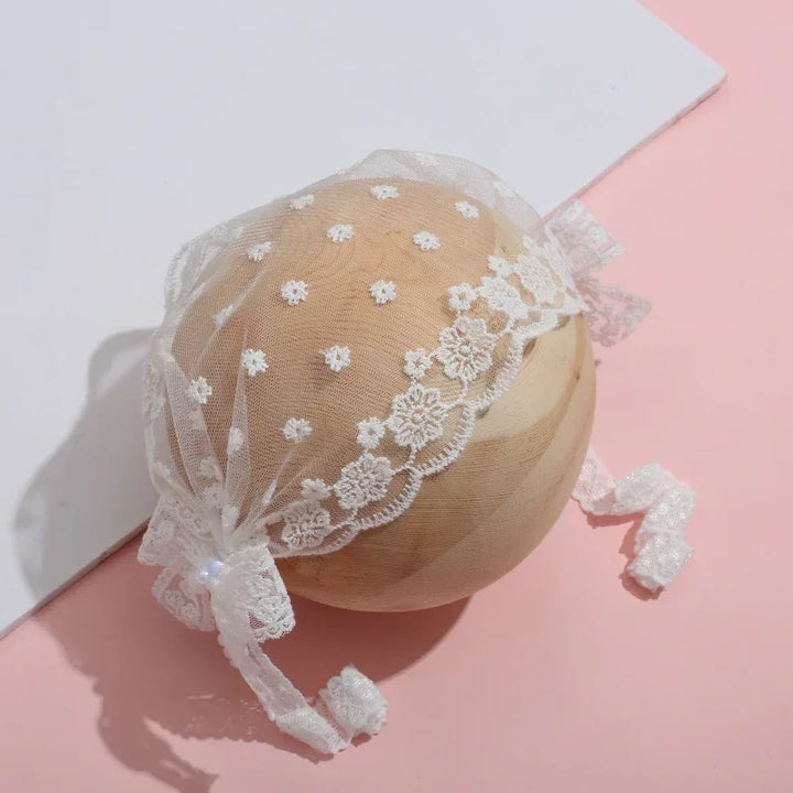 Delicate white lace bonnet with floral embroidery and ribbon ties on wooden sphere