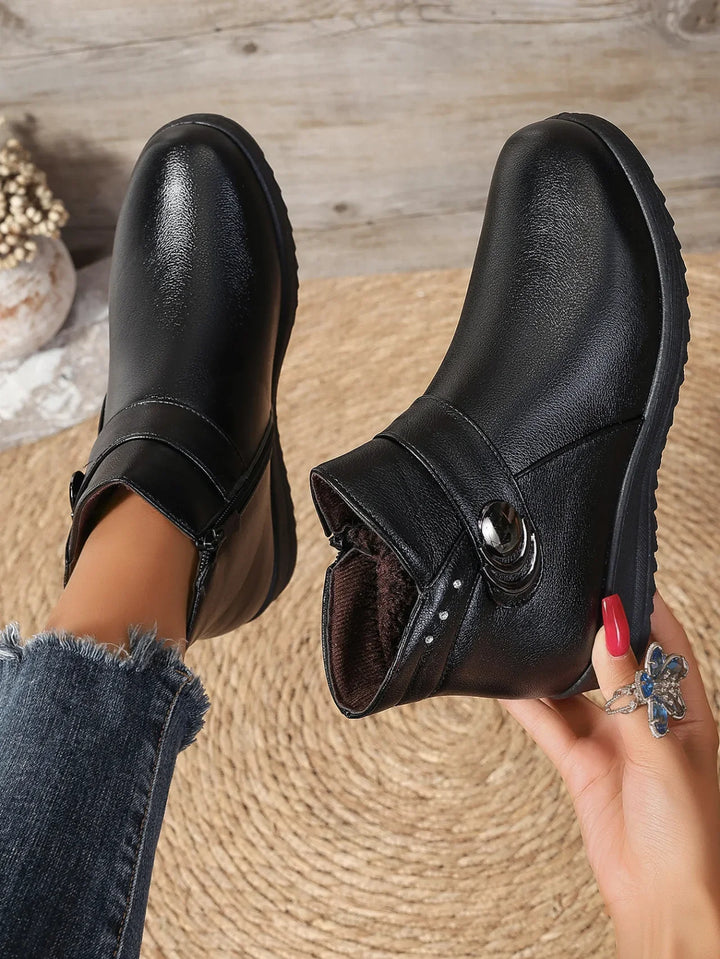 Black ankle boots with side zipper and decorative button detail on foot with frayed hem jeans