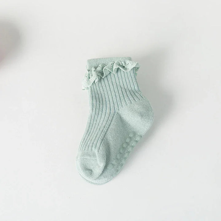 Light green ribbed baby sock with ruffled lace trim and non-slip dots on the sole