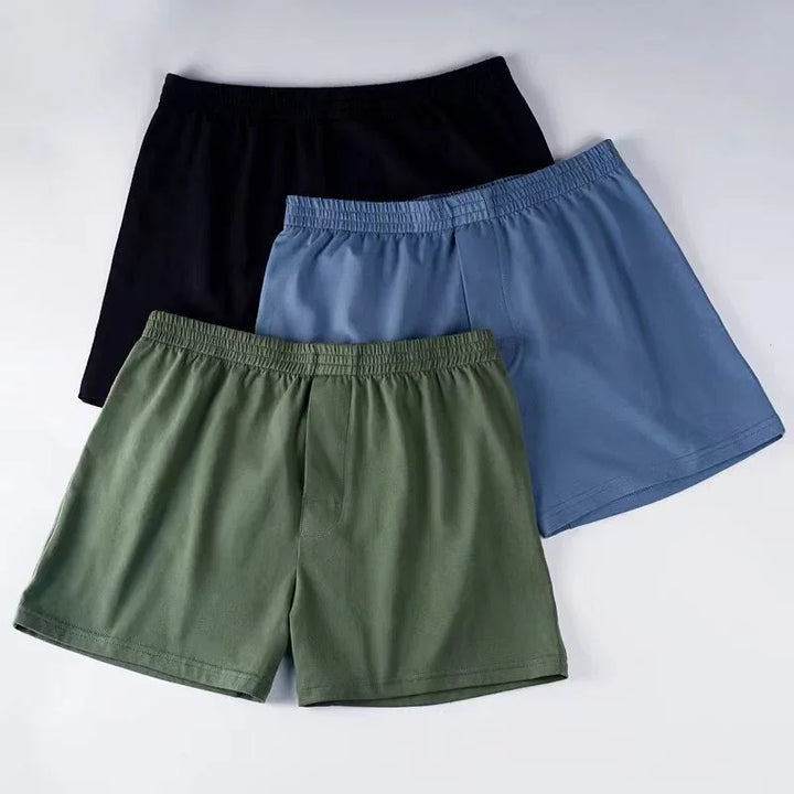 Three pairs of men's cotton boxer shorts in black, blue, and green colors with elastic waistbands