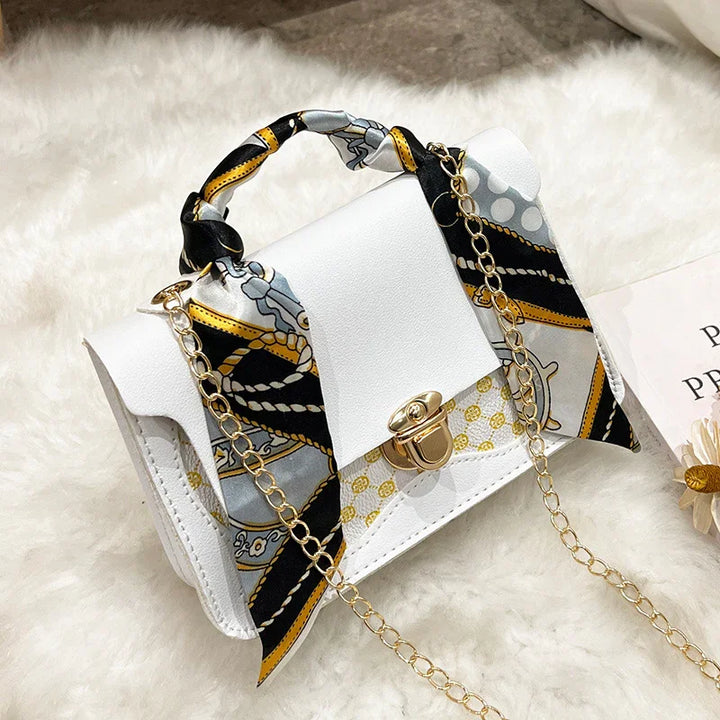 White leather handbag with gold clasp and chain, decorated with a black and gold patterned silk scarf