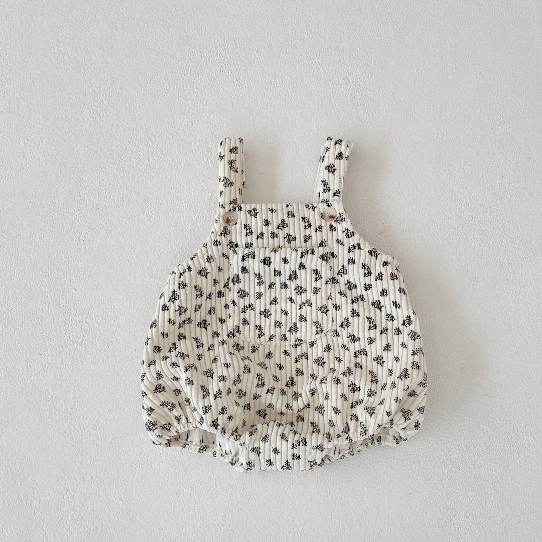 Baby romper with black floral print on white quilted fabric, adjustable shoulder straps with buttons