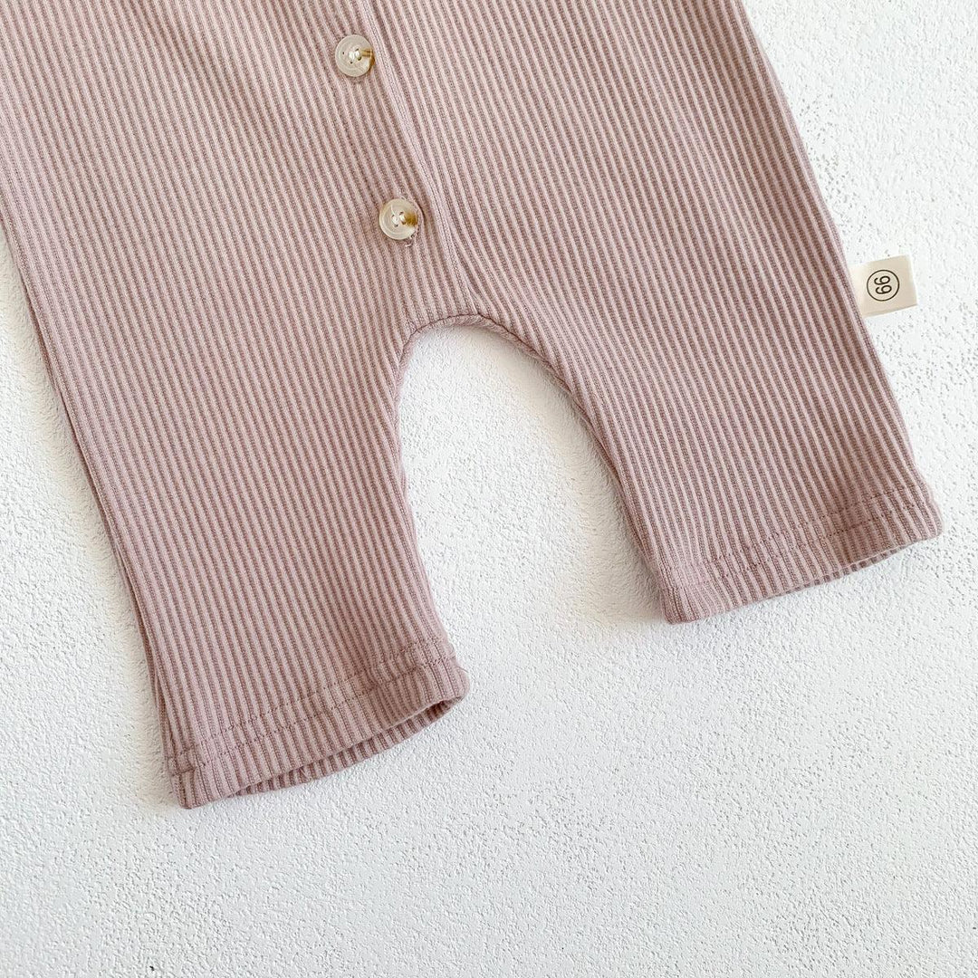 Close-up of beige ribbed baby romper with buttons and size tag on white textured surface