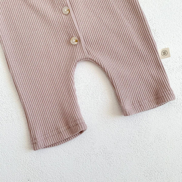 Close-up of beige ribbed baby romper with buttons and size tag on white textured surface