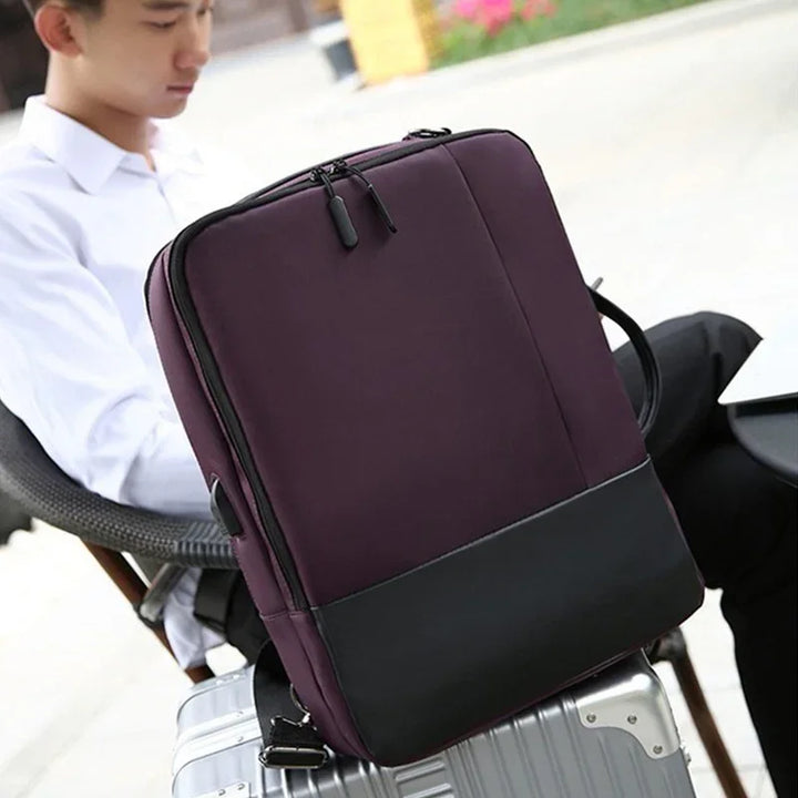 Purple and black laptop backpack resting on silver suitcase with person seated in outdoor cafe