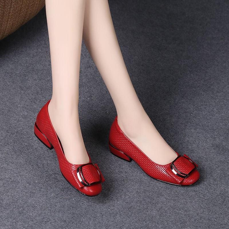 Women's red low-heeled textured leather shoes with large buckle detail on gray floor