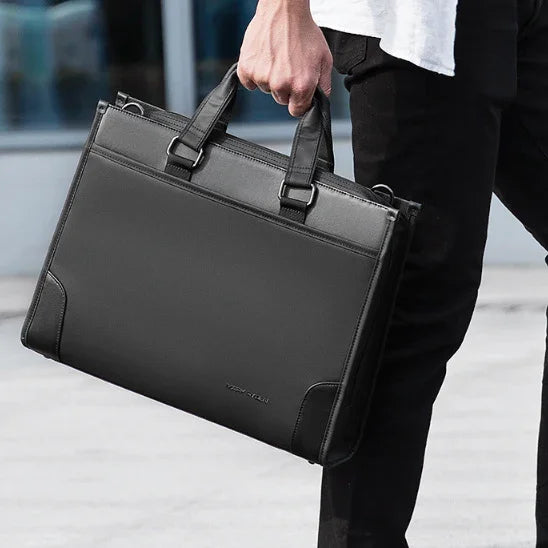 Person holding sleek black leather briefcase with handles, standing outdoors in casual attire