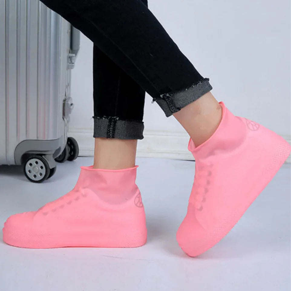 Person wearing bright pink waterproof shoe covers next to silver suitcase on white floor