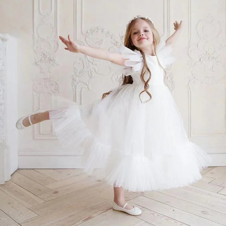 Young girl dancing in elegant white tulle dress with puffed sleeves and floral headband in bright room