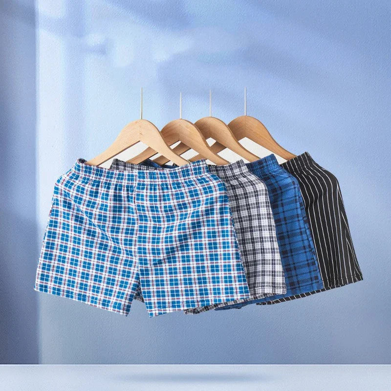 Set of four men's boxer shorts in blue and black patterns hanging on wooden hangers against a blue wall