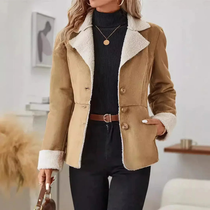 Woman wearing a tan shearling jacket with white fleece collar and cuffs over black turtleneck and black pants
