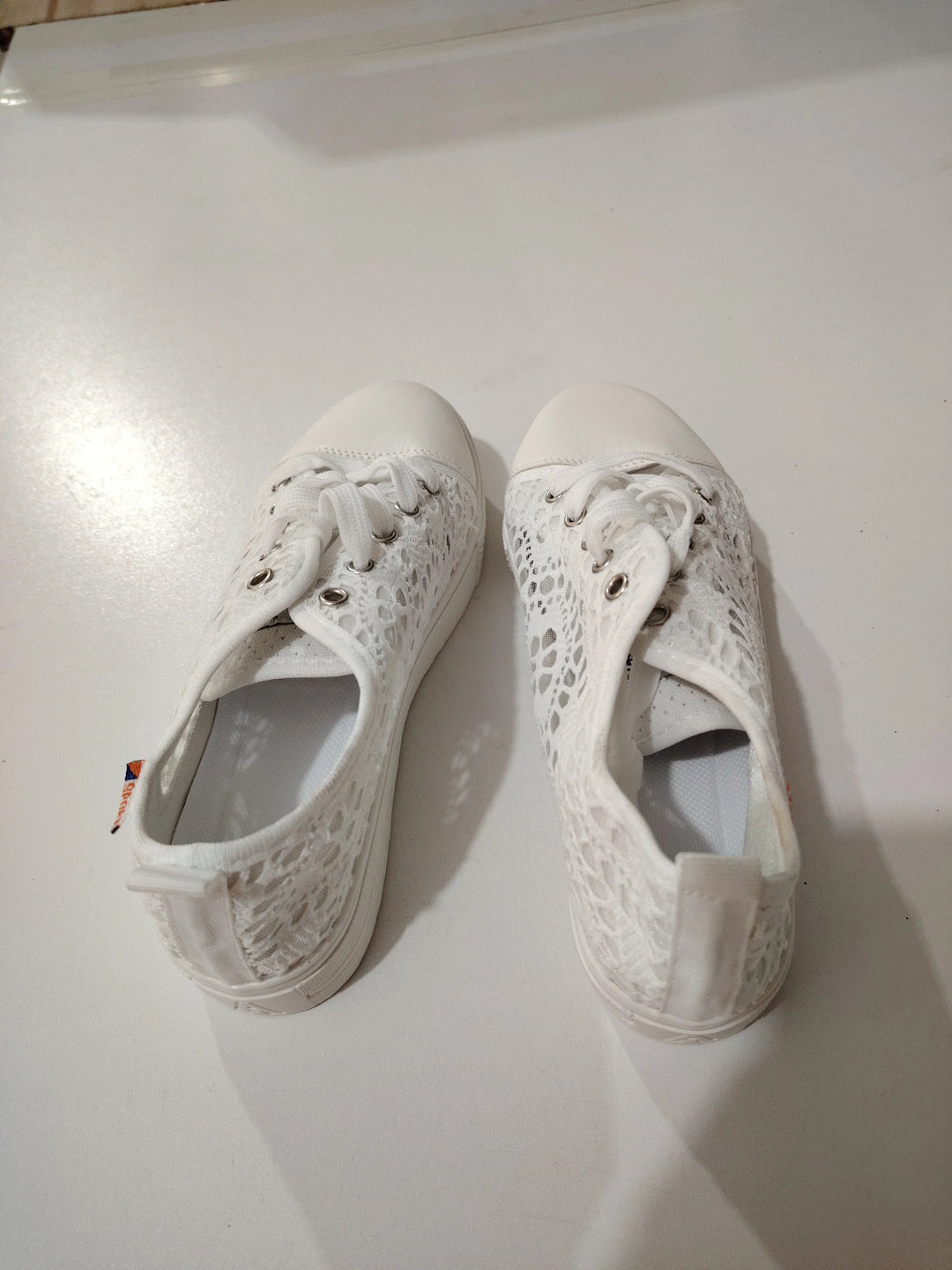 Pair of white lace casual sneakers with rubber toe caps and laces on a white surface