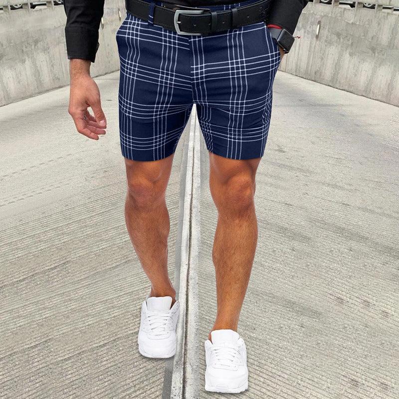 Man wearing navy blue plaid shorts, white sneakers, black belt, and black smartwatch on concrete pavement