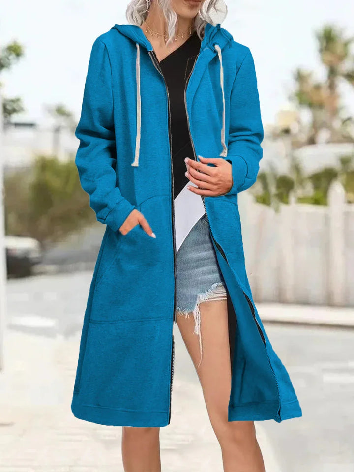 Woman wearing long blue zip-up hoodie with pockets over black and white top and ripped denim shorts outdoors