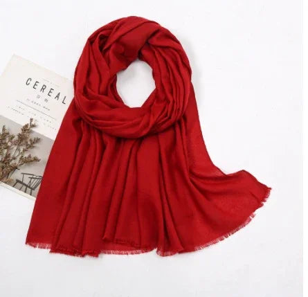soft red scarf with fringed edges displayed on white background next to a magazine and dried flowers