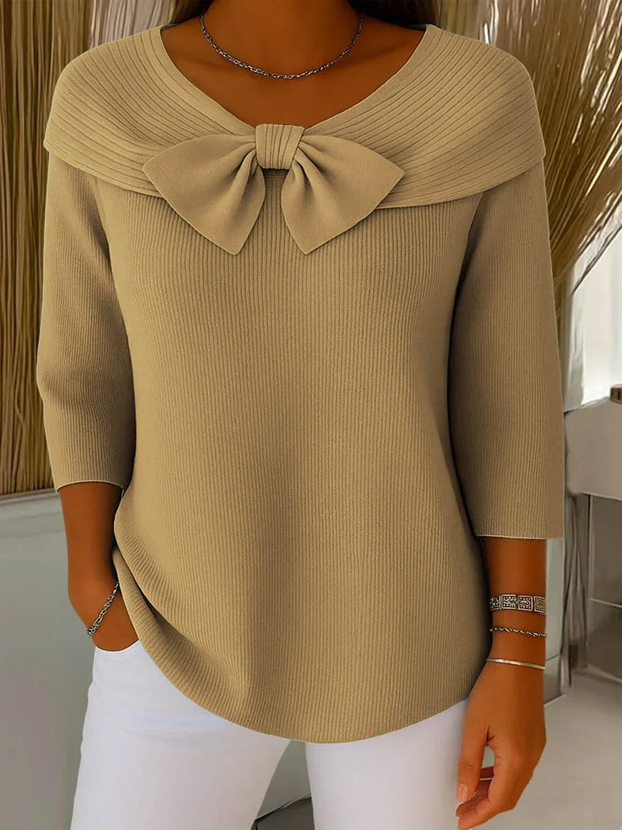 Beige ribbed knit sweater with large front bow and 3/4 sleeves, paired with white pants