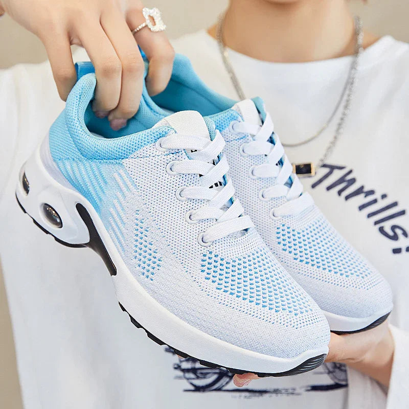 Close-up of white and light blue breathable mesh sports shoes held by a person wearing a white shirt and silver chain