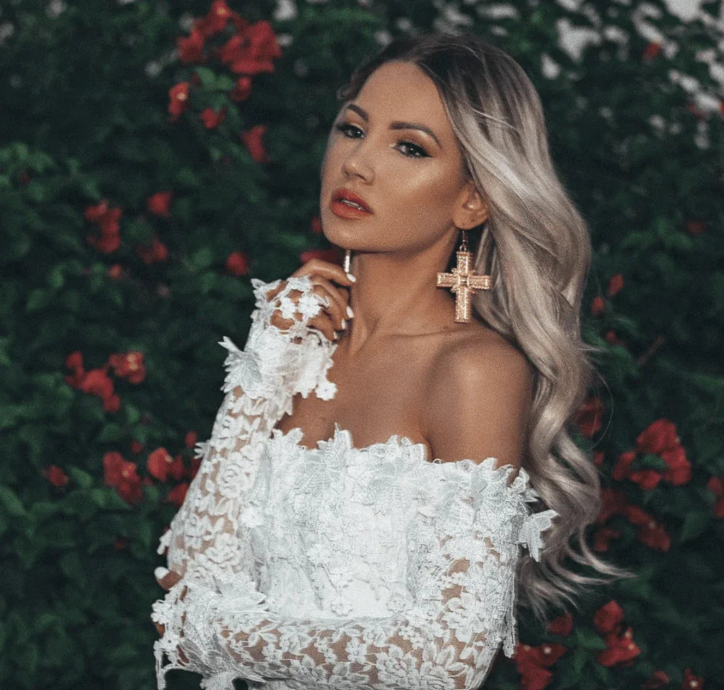 Woman with silver hair in white lace off-shoulder top posing against red flower bush background