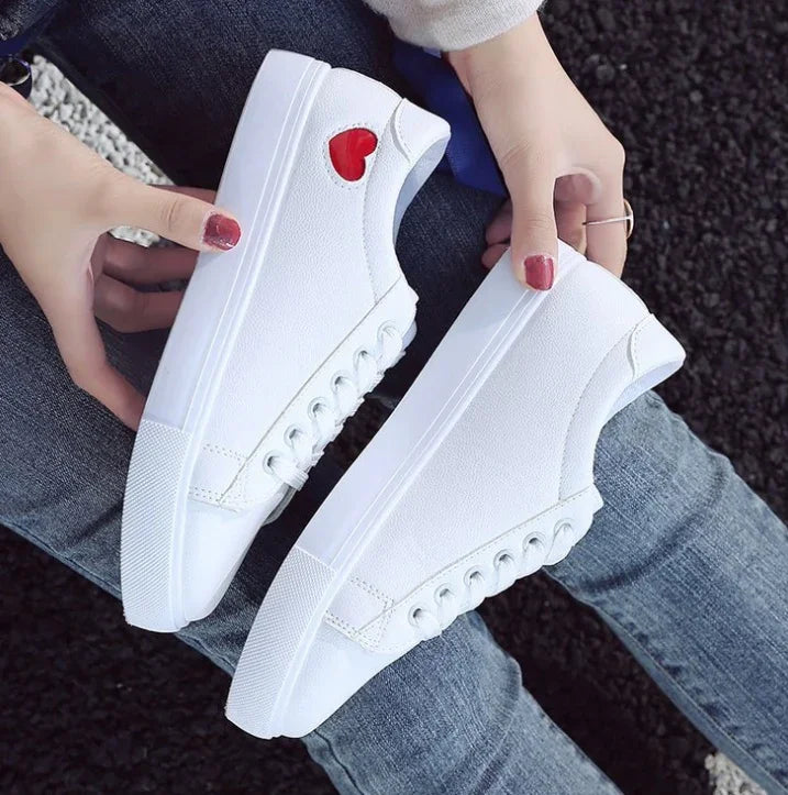 White canvas sneakers with red heart detail, held by person wearing jeans and sweater