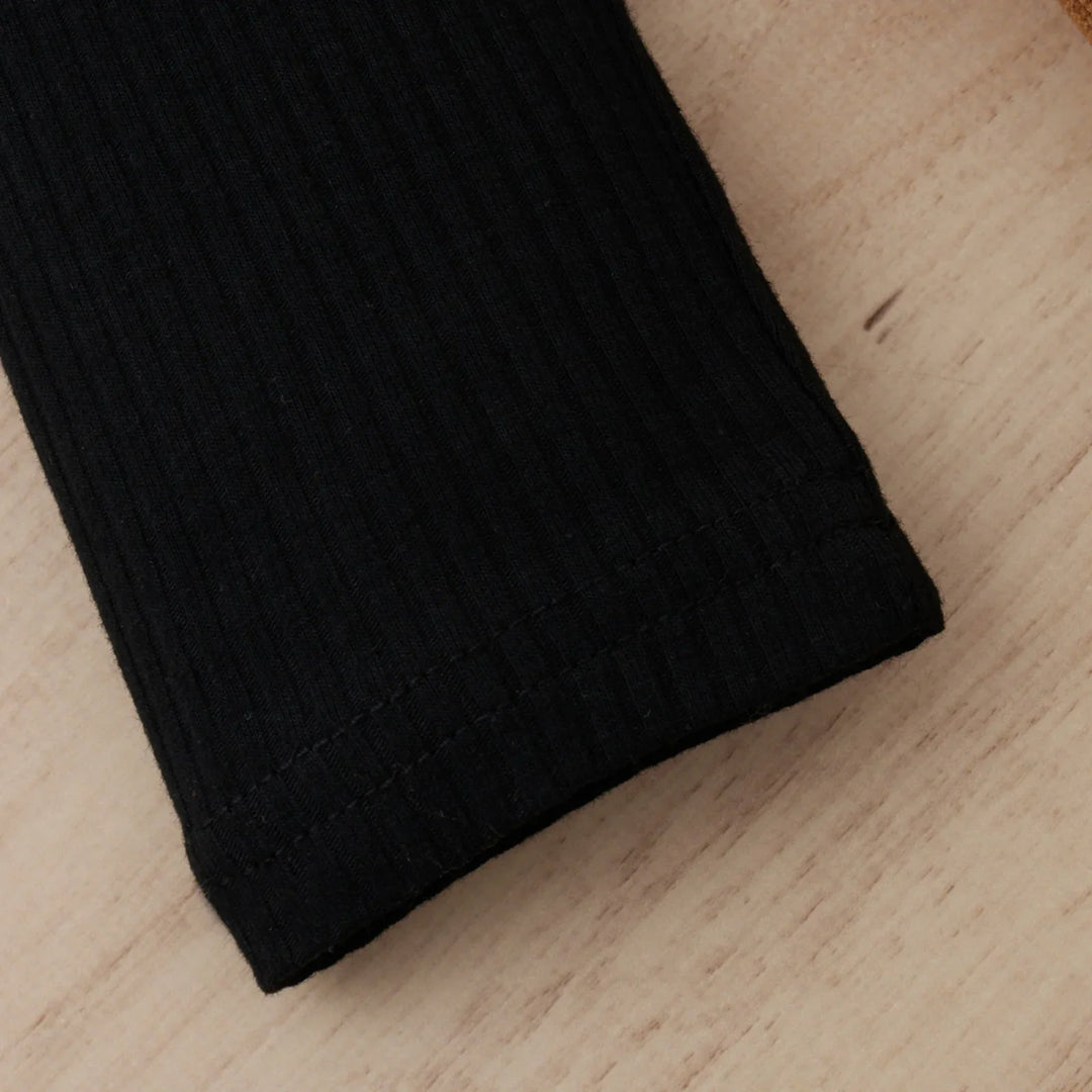 Close-up of black ribbed fabric sleeve with hem stitching on wooden surface
