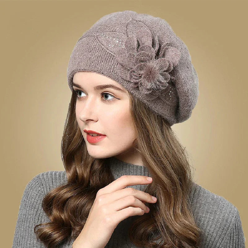 Woman wearing taupe knitted beret with floral decoration and gray sweater against beige background