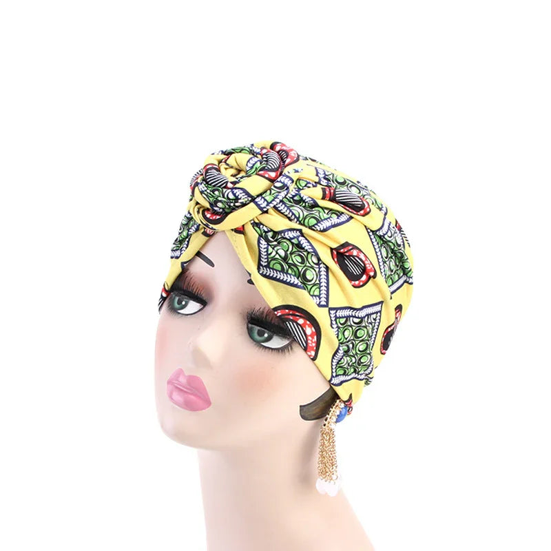 Mannequin head wearing a yellow African print turban headwrap with bold patterns and gold chain earrings