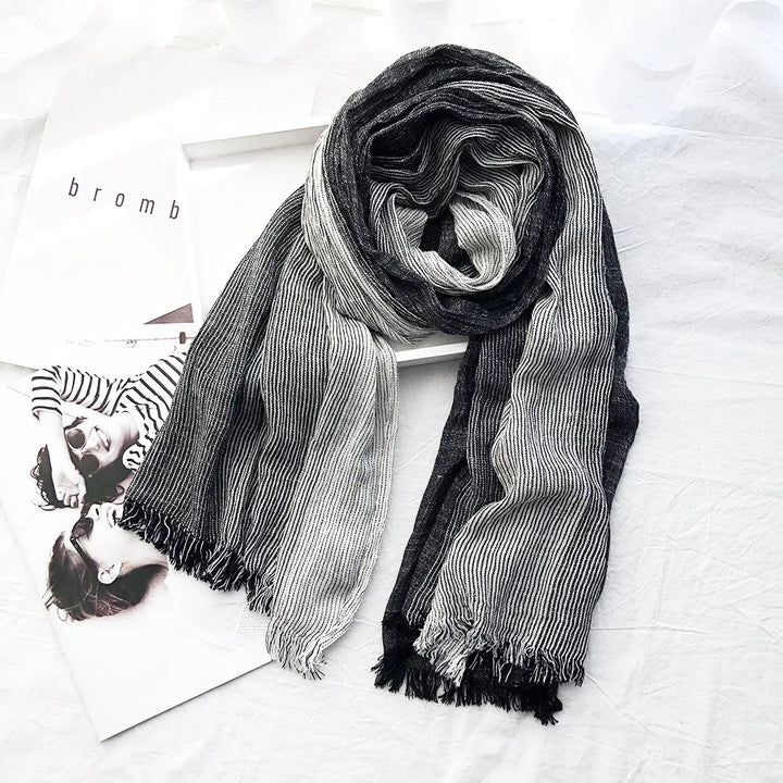 Black and white striped fringed scarf laid on white fabric with black and white magazine pages