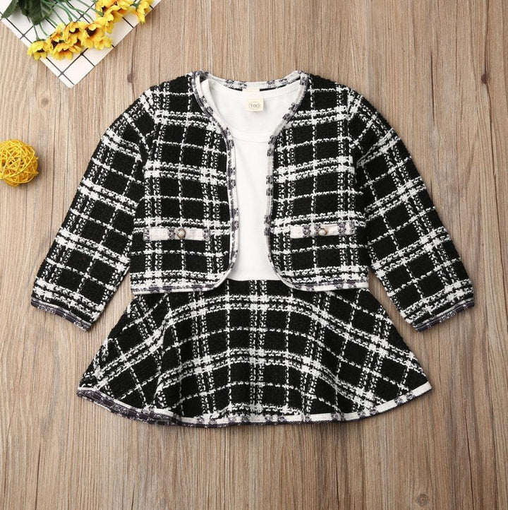 Black and white plaid toddler girl outfit with jacket, skirt, and white inner top on wooden floor