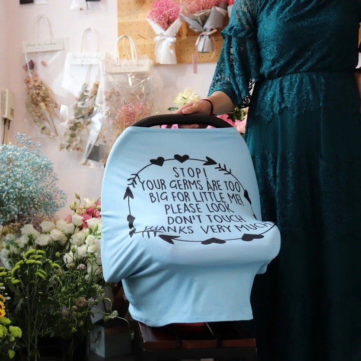 Baby car seat covered with a blue protective cover warning 'Stop! Your germs are too big for little me! Please look, don't touch' in a flower shop