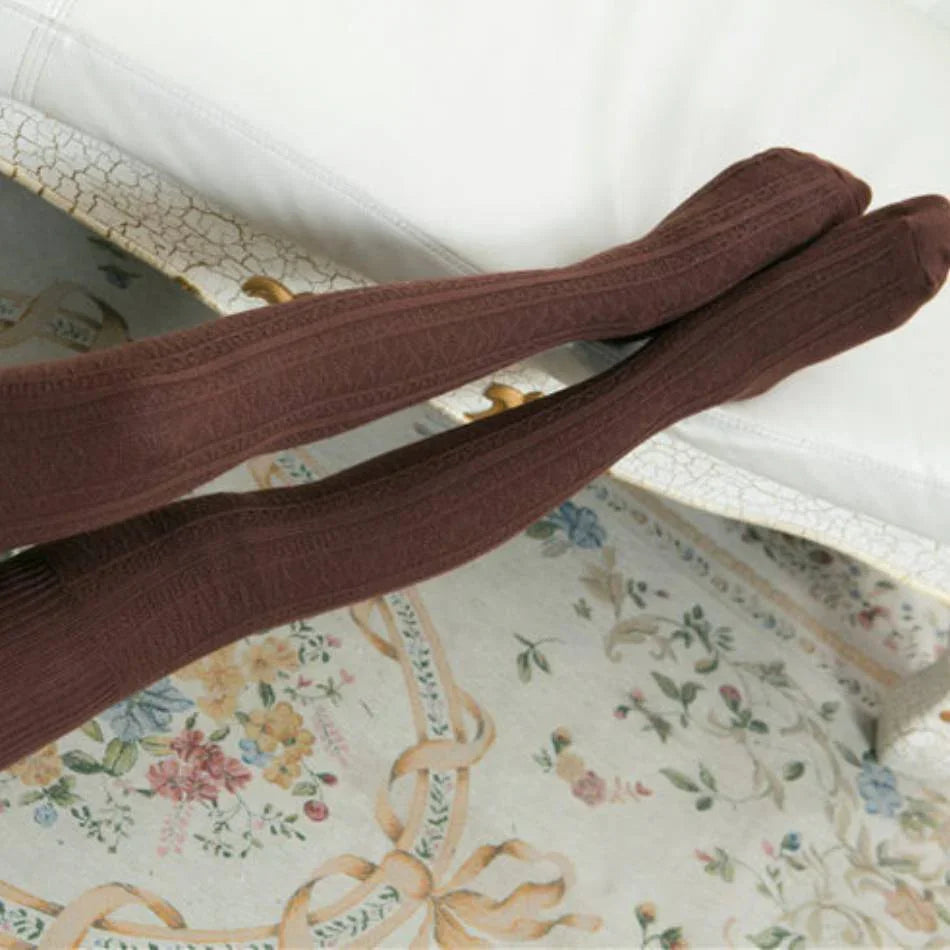 Brown cable-knit thigh-high socks worn indoors on floral patterned rug with vintage white furniture