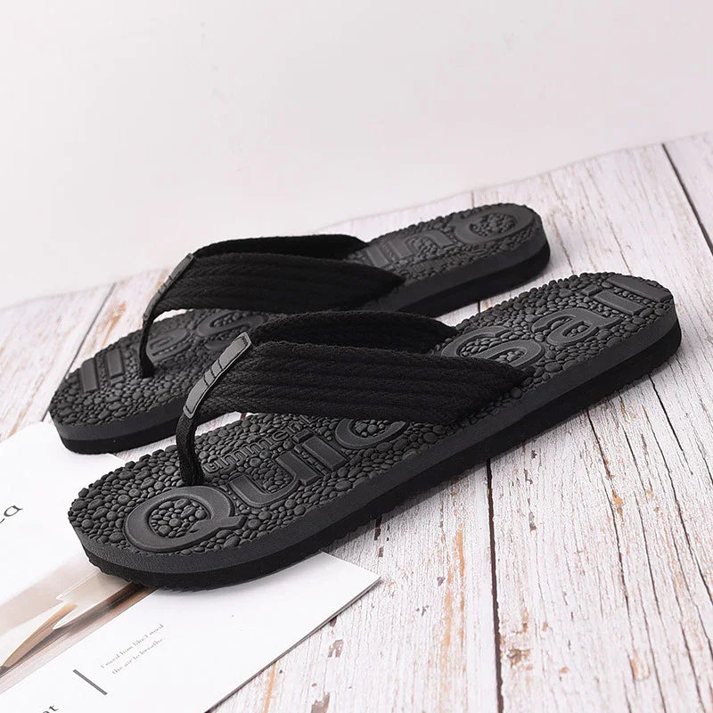 Black textured flip flop sandals with thick fabric straps on white wooden surface