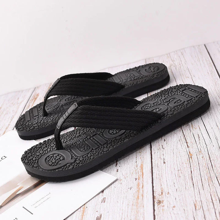 Black textured flip flop sandals with thick fabric straps on white wooden surface