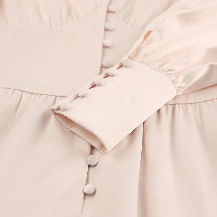 Close-up of light beige fabric dress with fabric-covered buttons and puff sleeve cuff detail