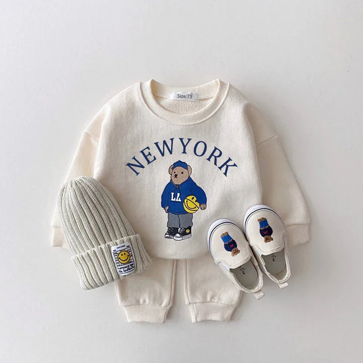 Cream toddler outfit with New York bear print sweatshirt, matching pants, knit beanie, and slip-on shoes