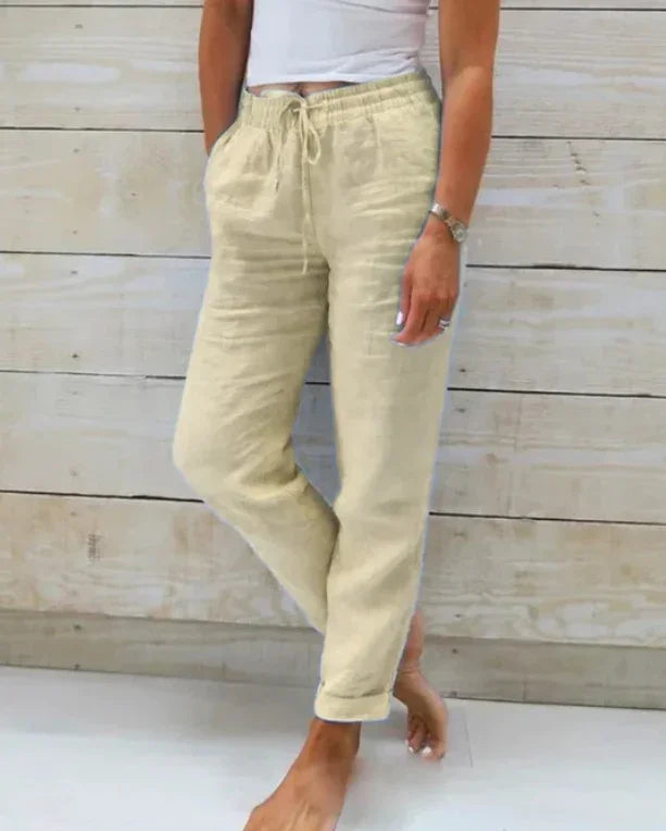 Woman wearing beige linen drawstring casual pants with rolled cuffs standing barefoot
