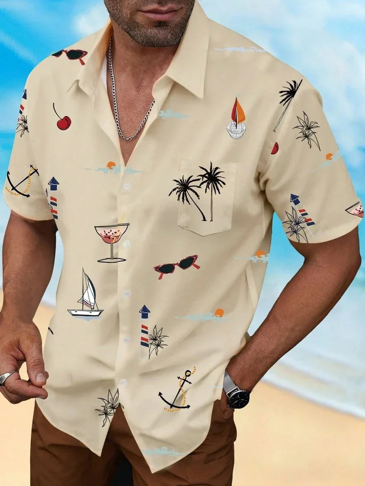 Man wearing beige tropical print short-sleeve shirt with palm trees, anchors, sailboats, and sunglasses