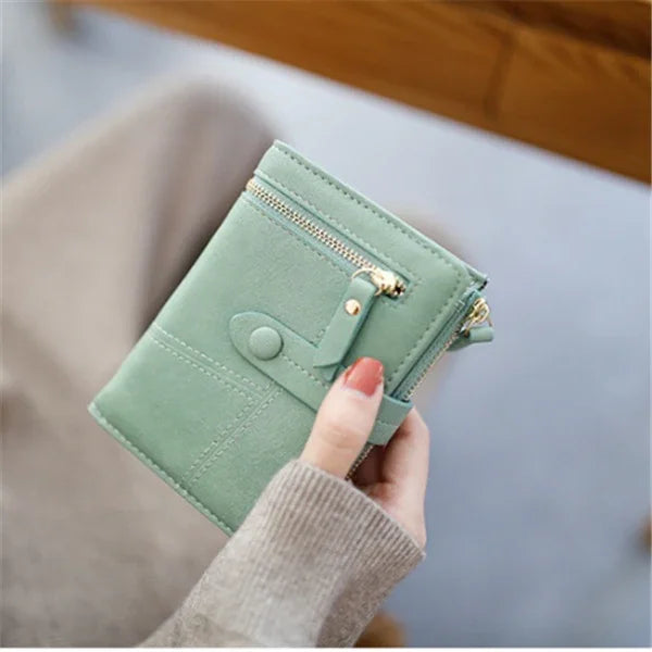 hand holding small green leather wallet with gold zipper and snap button closure