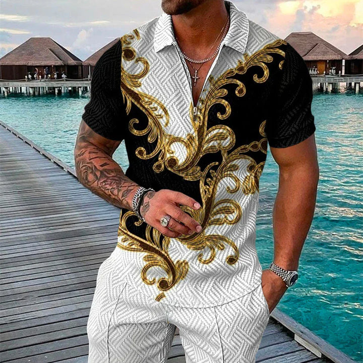Man wearing black and white short sleeve shirt with gold baroque patterns standing on wooden pier by overwater bungalows