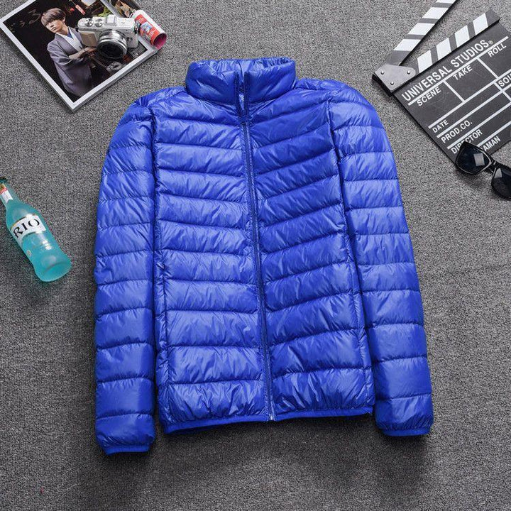 Blue lightweight puffer jacket with zipper lying on grey carpet beside magazine, clapperboard, sunglasses, and bottle