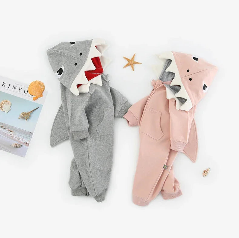 Gray and pink shark theme baby onesies with hoods featuring shark faces and fins, surrounded by seashells and starfish