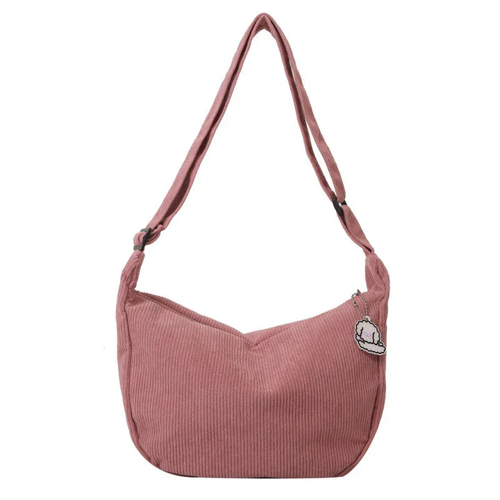 Pink corduroy shoulder bag with adjustable strap and small cat keychain on white background