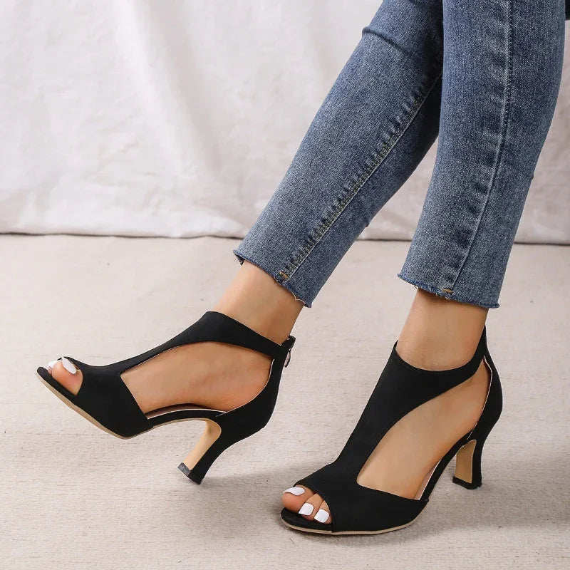 Black cutout high heel shoes worn with blue skinny jeans on light floor