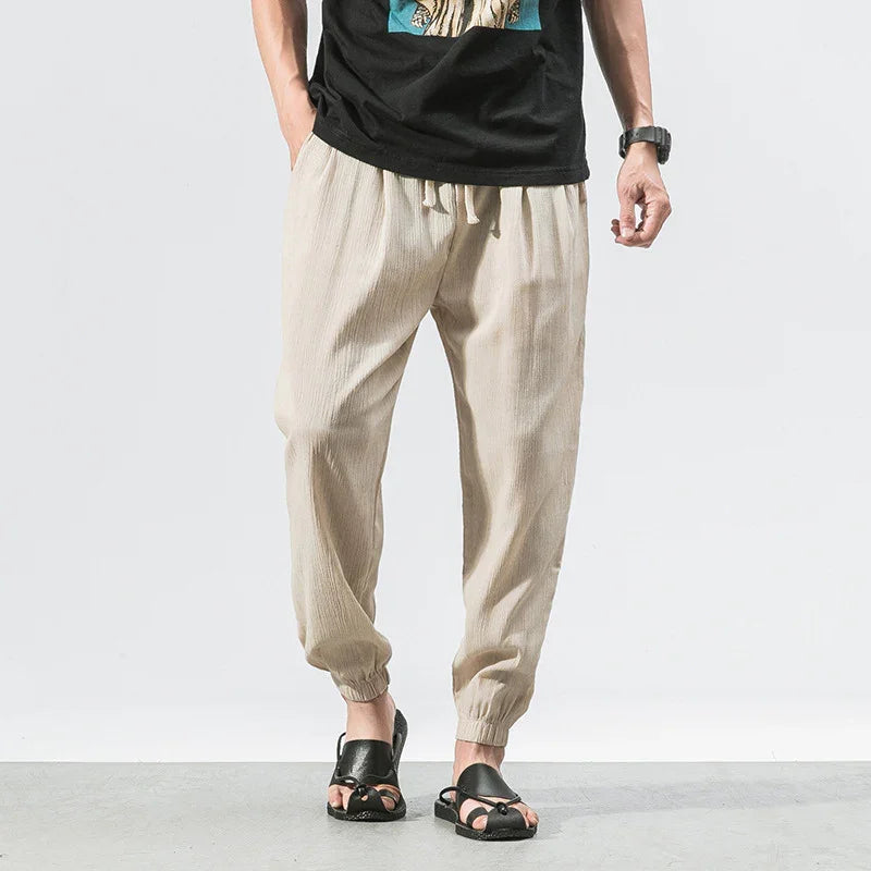 Man wearing beige casual jogger pants with elastic cuffs and black sandals on gray floor