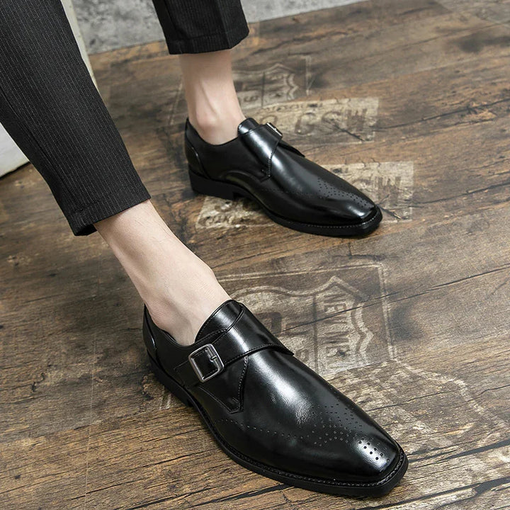 Mens black leather monk strap dress shoes worn with black pinstripe pants on wooden floor