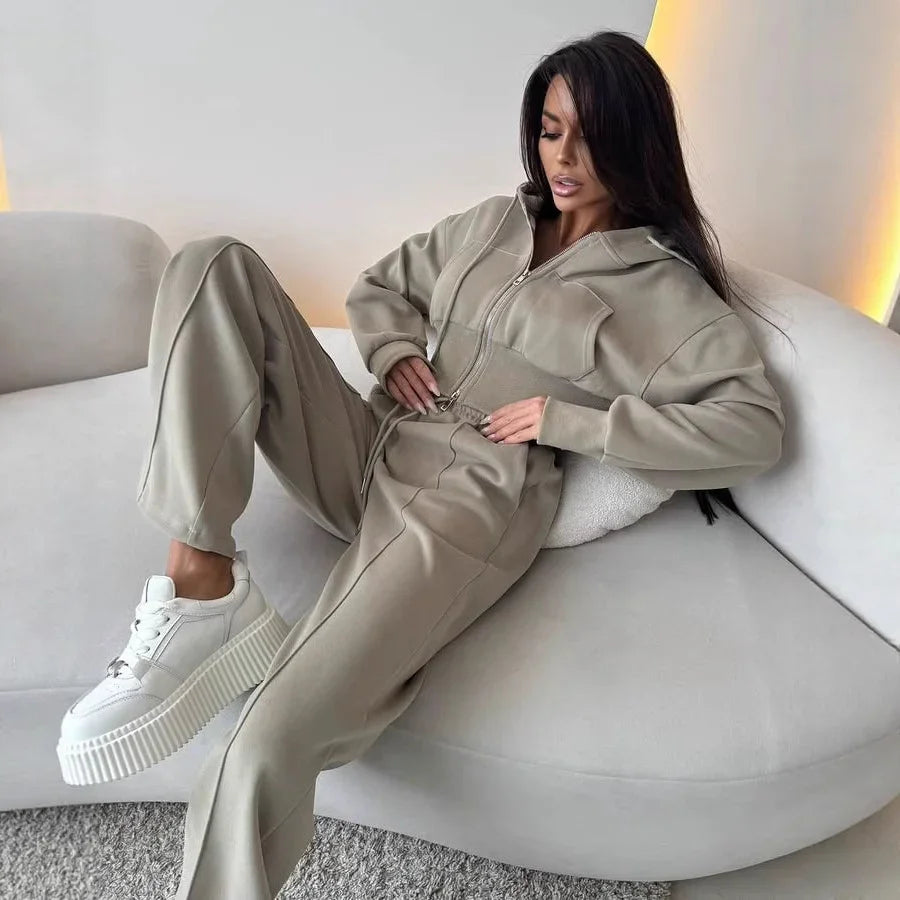 Woman lounging on a modern curved white sofa wearing beige zip-up hoodie, matching pants, and white platform sneakers