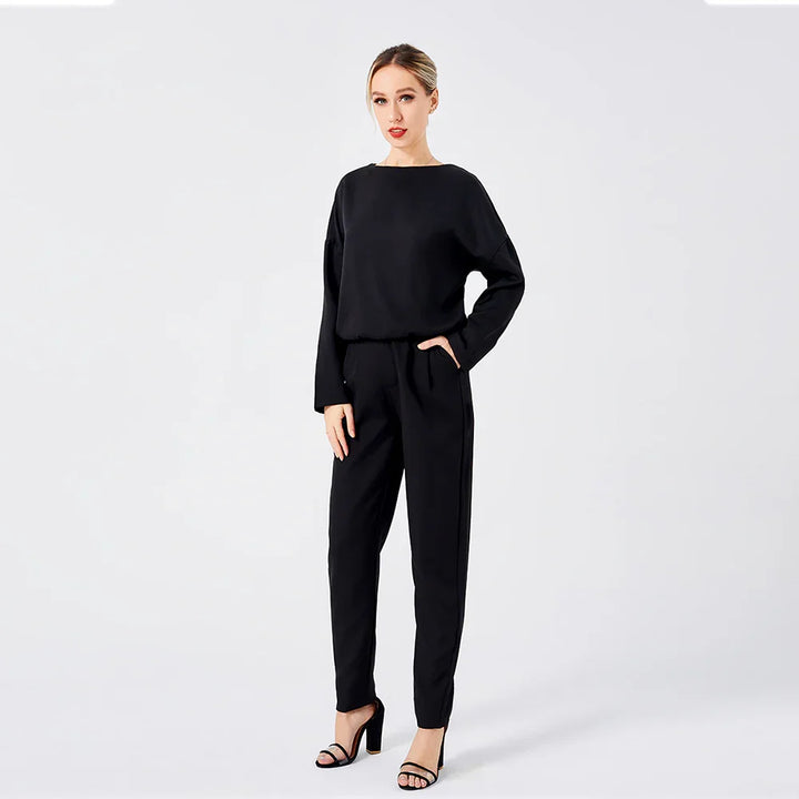 Woman in stylish black long-sleeve top and pants with high-heeled sandals on white background