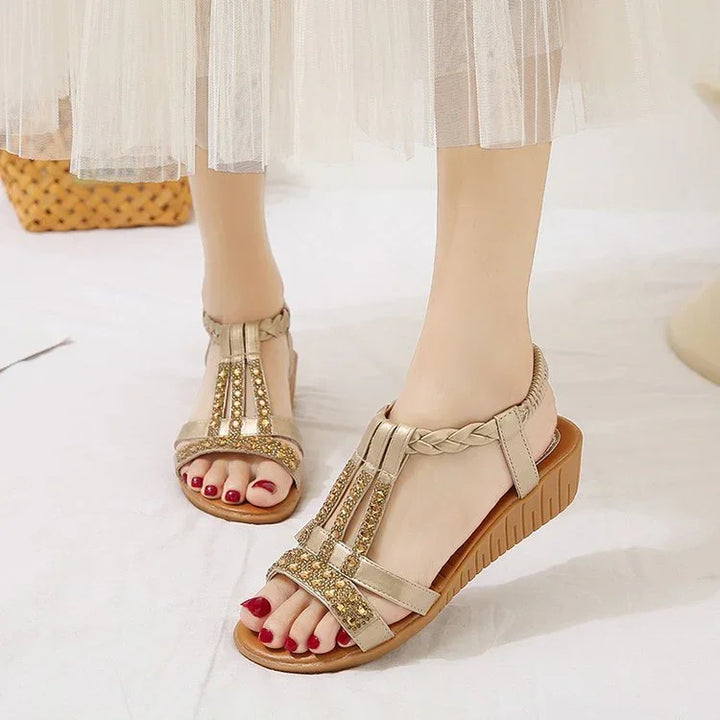 Woman wearing gold beaded T-strap wedge sandals with braided ankle straps and red pedicure