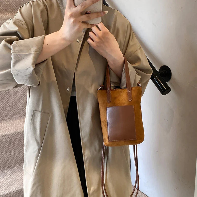 Woman in beige trench coat holding a small brown suede crossbody bag with leather pocket