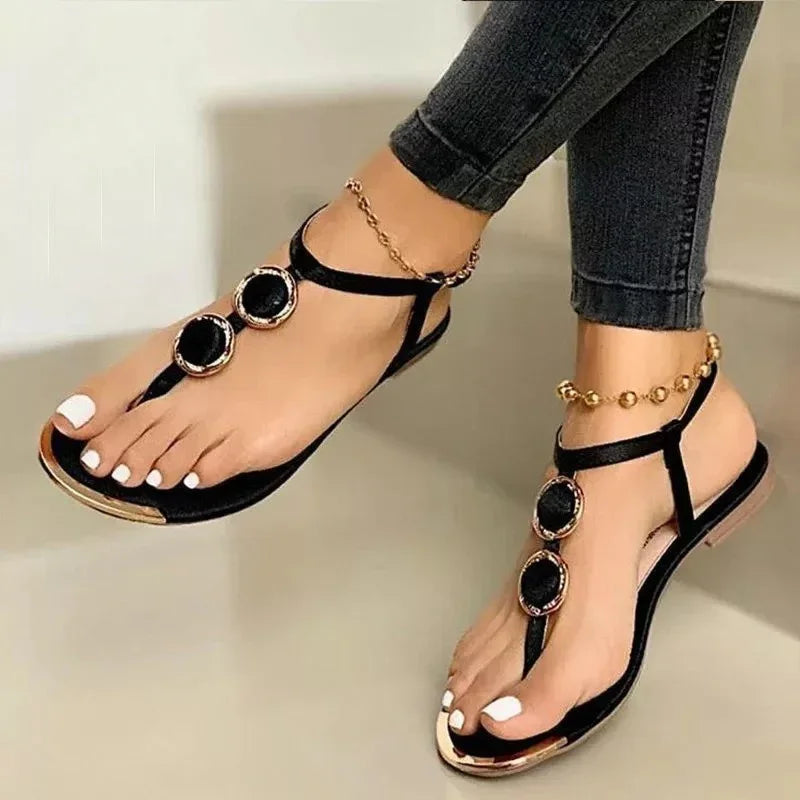 Black velvet flat sandals with gold details and round embellishments worn with ankle bracelets and black jeans